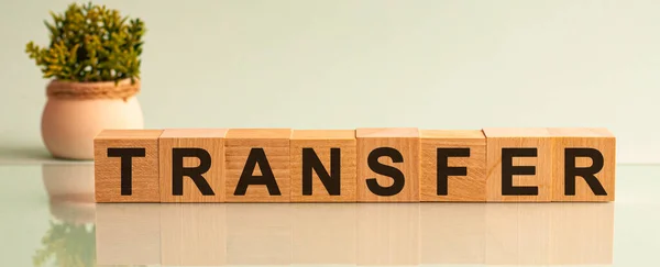 Transfer message word on a wooden desk on cube blocks with a flower on background. Transfer sign on a wooden table on brick background