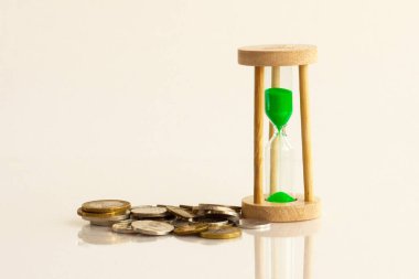 Sarı zemin üzerinde bozuk paralar olan kum saati..