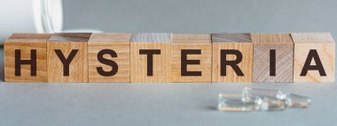 Kelime histerisi. Tahta bloklarda histerik yazı. Bir sıra küpün önünde ampuller, arka planda - tabletlerden alınan beyaz plastik ambalajlar, gri bir yüzey üzerinde yer almaktadır.