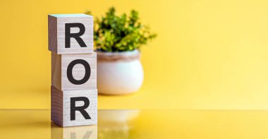 - Dönüş Oranı. Tahta bloklar, ROR kelimesi, sarı arka plan. Yüksek düzeyde iş karlılığı.
