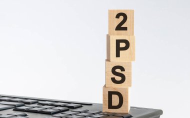 PSD2 - Tahta bloklardaki kısaltma harflerle, Ödeme Hizmetleri Direktifi 2 ödeme ve ticaret konsepti, beyaz arka planda ön görünüm.