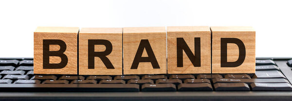 BrAND word made with building blocks jn the black keyboard. Ряд деревянных кубиков со словом, написанным черным шрифтом, расположен на черной клавиатуре.