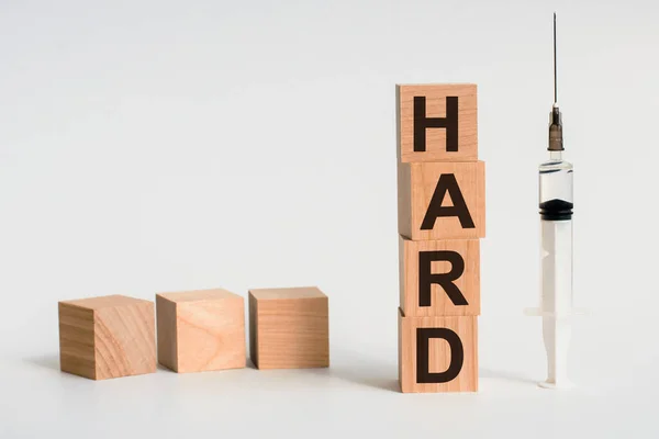 Slovo Hard Vytvořené Dřevěnými Kvádry Bílém Stole Vedle Injekční Stříkačka — Stock fotografie