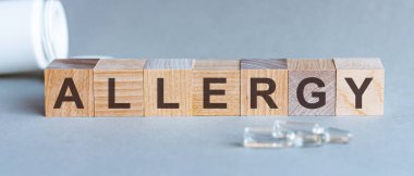 Tahta bloklardaki ALLERGY metni. Bir sıra küpün önünde ampuller, arka planda - tabletlerden alınan beyaz plastik ambalajlar, gri bir yüzey üzerinde yer almaktadır. Resmi Kabul Et