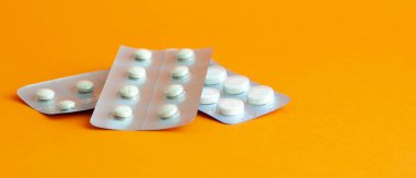Turuncu arka planda üç adet genel tablet kabarcığı. Plastik paketlerde çeşitli haplar. Ağrı kesiciler, hormonlar, antidepresanlar, aspirinler..
