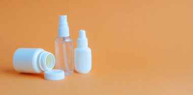 Tablet ve vitaminli üç taşınabilir plastik şişe ve masanın üzerinde dezenfektan antiseptik jel olan şeffaf bir plastik şişe. Turuncu desenli arkaplan.