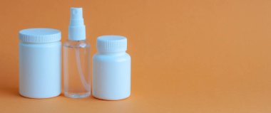 Tablet ve vitaminli üç taşınabilir plastik şişe ve masanın üzerinde dezenfektan antiseptik jel olan şeffaf bir plastik şişe. Turuncu desenli arkaplan.