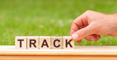 Sözcük Parçası tahta bloklarla yazılmış. Elinde tahta küp bloğu olan yeşil çimenlik arka planda TrACK iş sözcüğü olan bir adam.