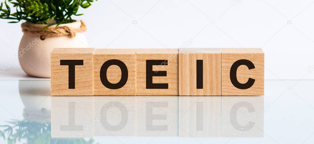 Toeic - acronym from wooden blocks with letters, abbreviation TOEIC Test of English for International Communication, concept, grey background with flowers. Toeic word on wooden cubes. Toeic concept