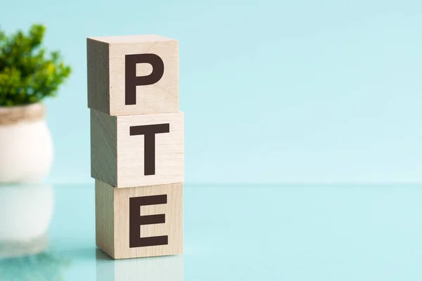 PTE - acronym from wooden blocks with letters, Pearson Tests of English PTE concept Foreign Language exams. Blue background