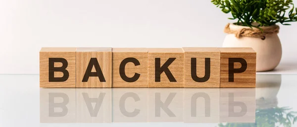 キューブ上のBackupのテキスト 背景に花の付いた立方体ブロック上の木製の机の上のBackupメッセージワード — ストック写真