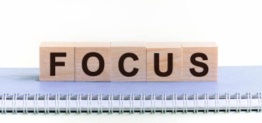FOCUS - siyah harfli ahşap bloklardan oluşan bir kelime, mavi bir Notepad üzerinde bir sıra blok bulunuyor. Beyaz arka plan, ön manzara. Hedef kodu, tanıtım kodu kavramı.