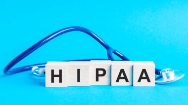 HIPAA kelimesi yapı taşlarından yapılmış. Üzerinde kelime virüsü olan tahta blok masada steteskop, sigorta ve tıbbi konsept, mavi arka plan