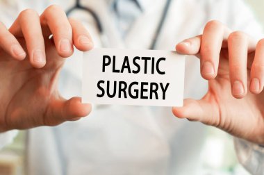 Doktorun elinde Plastiksel SÜRGERY yazılı bir kart var. Tıbbi konsept.