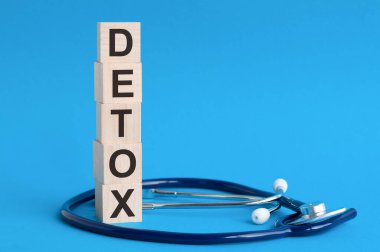 Tahta bloklara ve açık mavi arka plana steteskop üzerine yazılmış Detoks kelimesi, sigorta ve tıbbi konsept