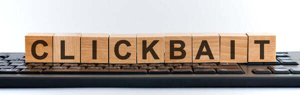 Clickbait word made with building blocks. A row of wooden cubes with a word written in black font is located on a black keyboard.