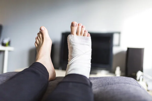 Uomo davanti alla TV con una gamba rotta — Foto Stock