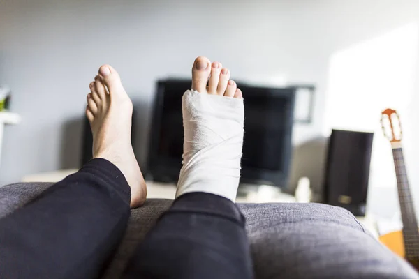 Homme devant le téléviseur avec une jambe cassée — Photo