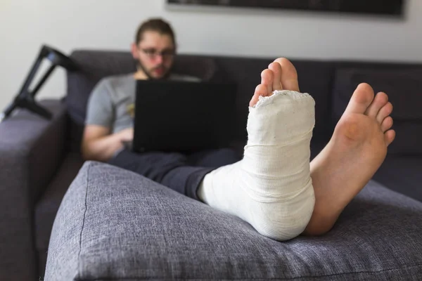 Homem com uma perna quebrada está navegando na internet — Fotografia de Stock