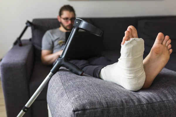 Homem com uma perna quebrada está navegando na internet — Fotografia de Stock