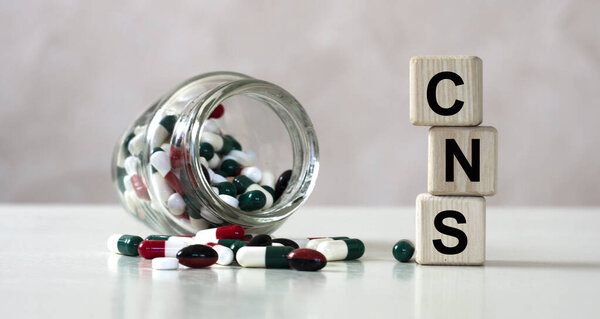 CNS (Central Nervous System) - acronym on cubes on a light background with a capacity with tablets. Medical concept
