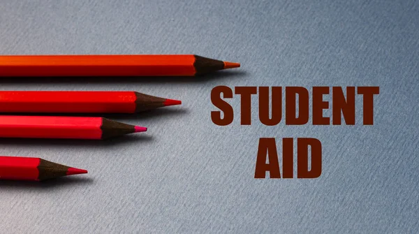 STUDENT AID - text on gray paper with red pencils lying next to. Finance and education concept