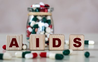 Kısaltma AIDS (Edinilmiş Bağışıklık Yetmezliği Sendromu) - bir kavanoz hapla arka planda tahta küplerle ilgili bir metin. Tıbbi konsept.