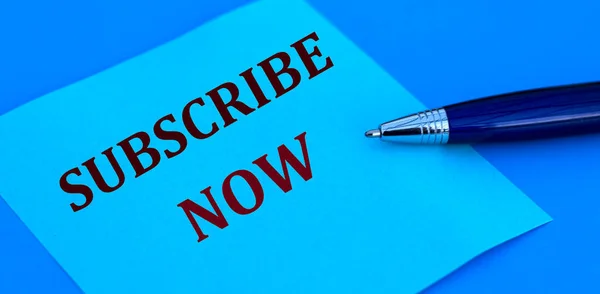 SUBSCRIBE NOW words written with a pen on blue paper on a blue background.