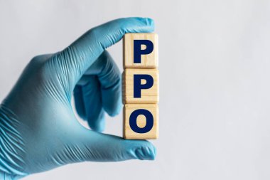 PPO (Preferred Provider Organization) is an acronym on cubes held by a hand in a blue glove. Medical concept. clipart