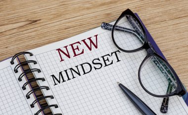 NEW Mindset - bir deftere yazılmış gözlük ve tahta arka planda bir kalem ile