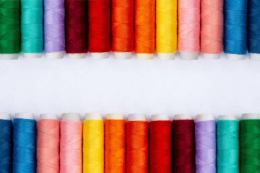 Beyaz arkaplanda renk dikiş iplikleri, üst görünüm. Dikiş Üretimi. Farklı renklerde iplikçiklerin sıraları. Tekstil endüstrisinde renkli iplik ruloları. İyi fikir. İplik