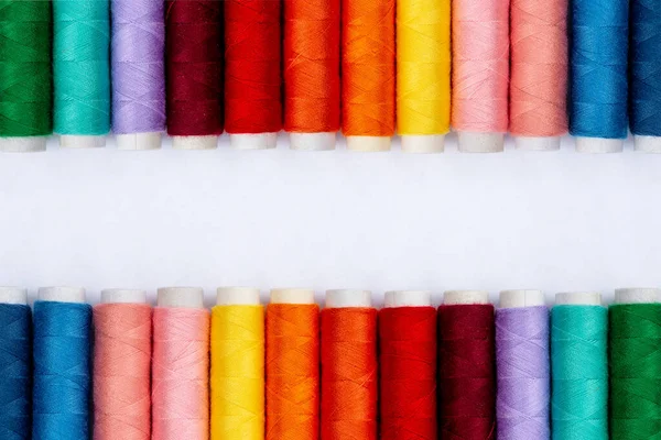 Filati per cucire a colori su sfondo bianco, vista dall'alto. Produzione di cucito. Righe di bobine di filo in colori diversi. Rotoli colorati di filo colorato nell'industria tessile. Idea dello striscione. Filettatura — Foto Stock