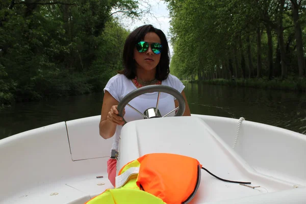 a young woman driving a small boat on the canal du midi in France