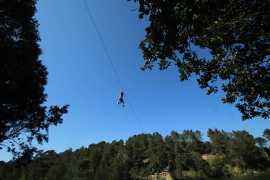 Macera parkında kablo boyunca kayan genç bir kız. 
