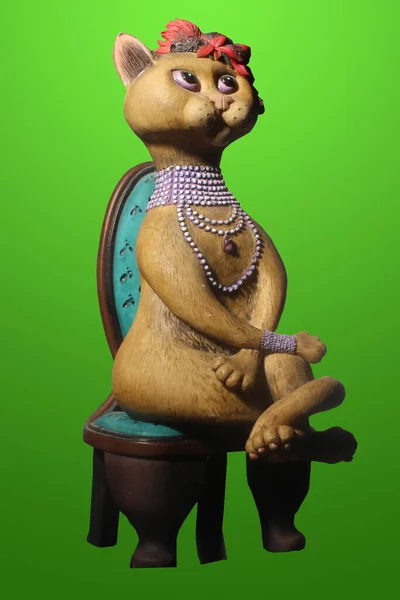 a terracotta statuette of a cat with a collar and a hat sitting on a wooden chair