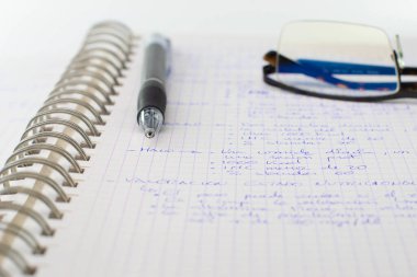 Metalik sarmal defter, üzerinde kalem ve gözlük var.