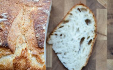 Kesilmiş bir ekmek yığınının bulanık arka planında bir somun taze ekmek. Tahta bir masanın üzerinde kızarmış ekmek ve fotokopi alanı..