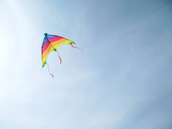 Fly a kite in the wind against clear blue sky with copy space. Close-up view of the striped rainbow kite flying in the sky on line. Freedom concept.