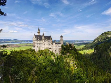 Bavyera 'nın yeşil dağlarındaki eski güzel Neuschweinstein şatosuna karşı samimi köyler, tarlalar, bir göl ve mavi bir gökyüzü. Neuschwanstein Kraliyet Kalesi Bavyera, Almanya.