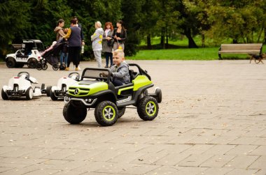 Kiev / Ukrayna, 3 Ekim 2020. Kafkasyalı küçük çocuk parkta elektrikli araba sürüyor. Sıcak bir sonbahar gününde çocuklarla açık havada aktif eğlence. Çocuklar için araba kiralama. Mutlu çocukluk kavramı.