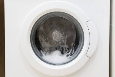 Çamaşır makinesi kapısı ve içinde dönen giysiler.