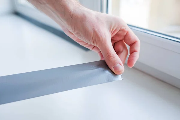 Worker putting sealing tape on window in house