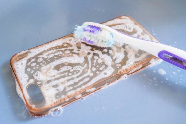 Cleaning the silicone phone case with toothbrush, foam and soap clipart
