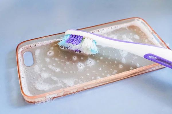 Чистка силиконового телефона с помощью зубной щетки, пены и мыла — стоковое фото