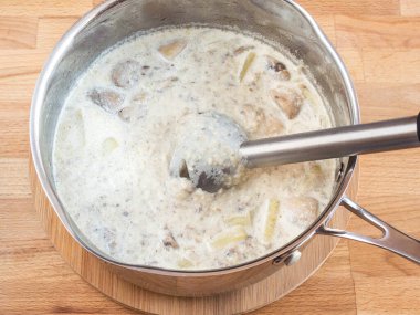 Tavada krema çorbası. Çorbanın içinde blender porsiyonu. Püre çorbası malzemelerini öğütün. Mantar ve patates parçaları.