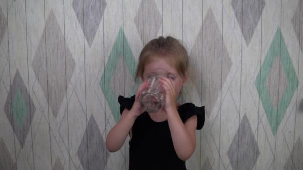 Маленькая девочка в черном платье пьет воду. — стоковое видео