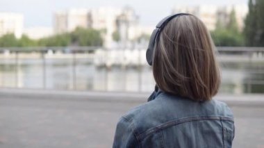 Kadın bankta oturuyor ve kulaklıkla müzik dinliyor.