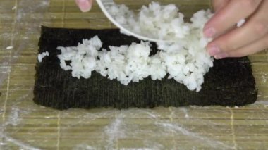 Kadın nori yaprağına pirinç koyar. Evde suşi pişiriyorum. Yakın çekim.