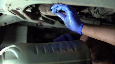 Bir adam arabanın motorunun altındaki vidayı söker ve yağı bir konteynıra boşaltır. Araba bakımı. 4k