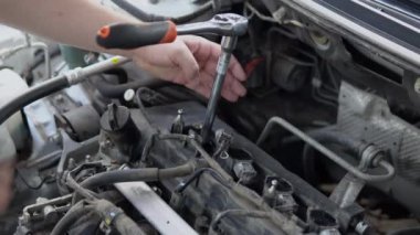 Bir adam eski bir bujiyi bir aletle arabanın motorundan söker.